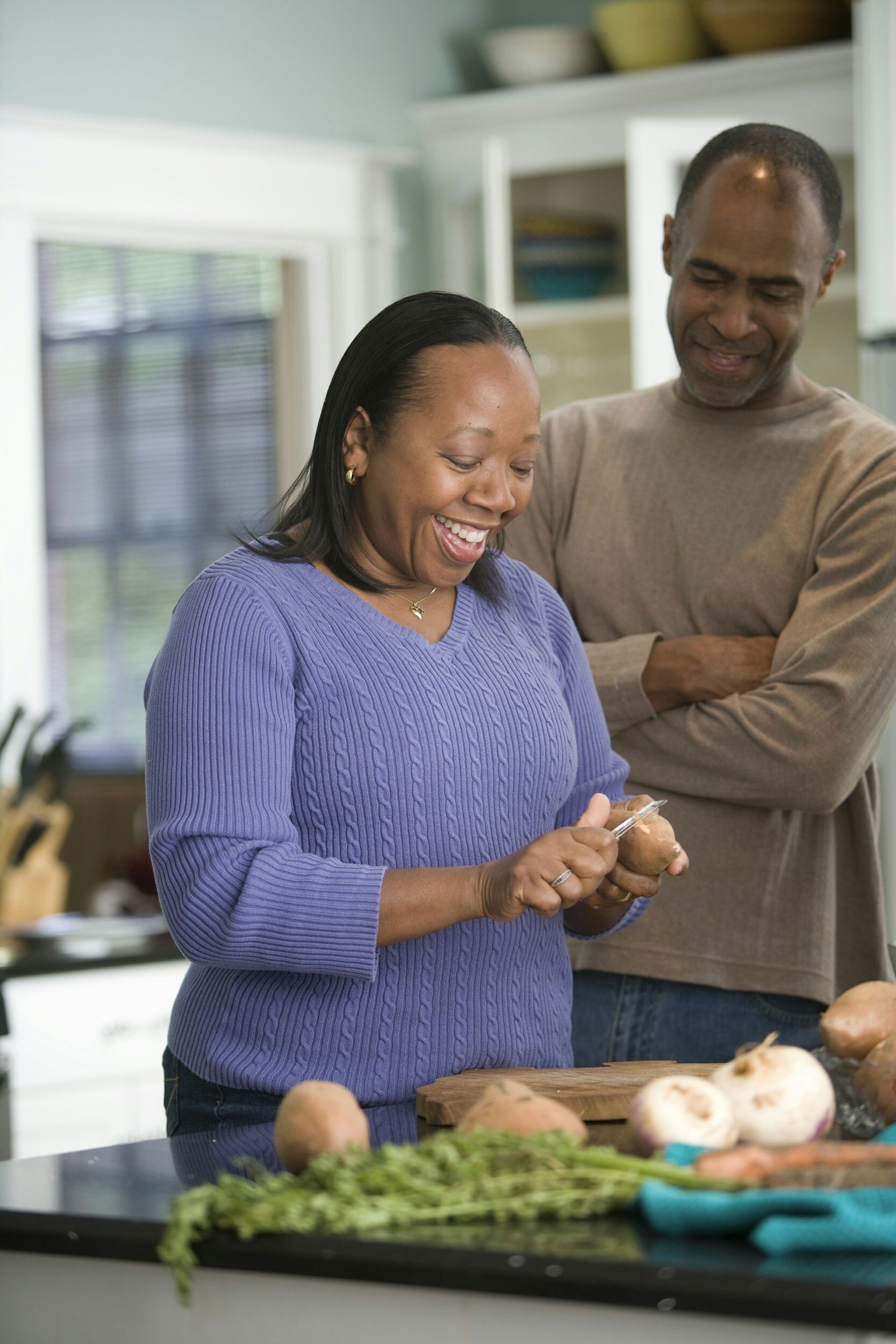 woman peeling a potato while a man stands behind her